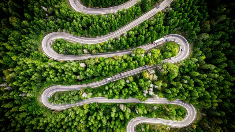 O dronă aeriană de sus în jos surprinde curbele dramatice de serpentine ale unui drum de munte care se învârte prin pădurile luxuriante și veșnic verzi din Munții Carpați de lângă Cheia, România