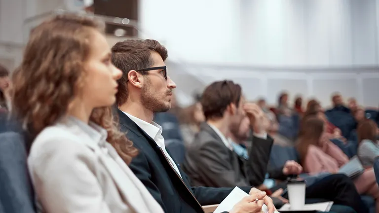 Young business people listening to a lecture from a financial event in a conference hall.