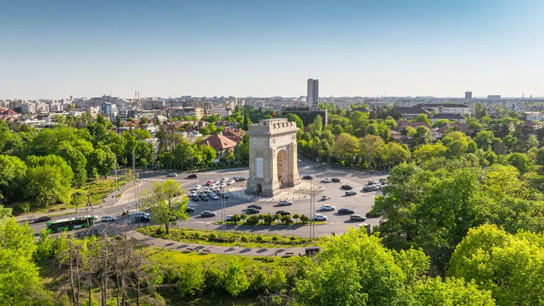The Arc of Triumph in Bucharest, Romania, surrounded by green nature, trees and buildings