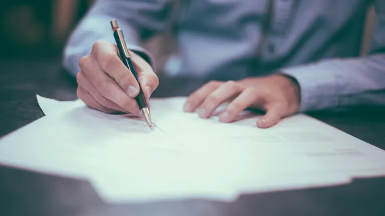 A man following information on printed papers with his black and gold pen