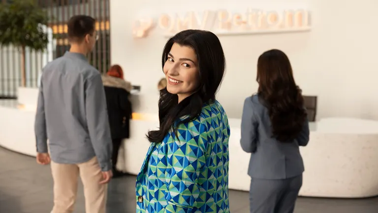 Young OMV Petrom female employee inside OMV Petrom headquarters smiling towards the camera. Company logo is visible in the background